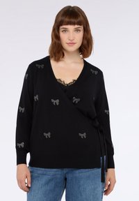 Svart insvepningströja med långa ärmar, prydd med silverfärgade rosettdekorationer, djup V-ringning och knytdetalj vid midjan. Mjuk stickad tyg.