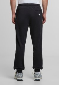 Sorte joggebukser laget av myk stoff, med elastisk midje, smalnettermanchetter og en enkelt baklomme med en liten logodetalj.