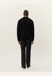 Schwarzer Pullover mit hohem Kragen und geripptem Textur, kombiniert mit grauen Hosen. Das Outfit ist für eine lockere Passform konzipiert.