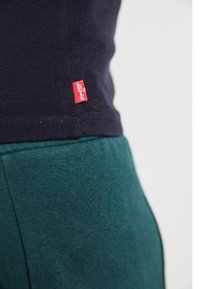 Marineblå T-skjorte stoff med en liten rød Levi's-lapp ved kanten, kombinert med grønne bomullsbukser som viser en myk tekstur og tettsittende passform.