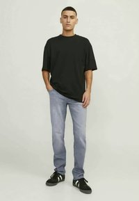 Svart oversized t-shirt, ljusblå denimjeans och svarta sneakers med vita ränder. Modellen står rak med händerna i fickorna.