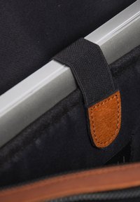 Interiorul unei genți negre din material textil, cu un accent din piele maro și o curea neagră, care asigură un obiect metalic argintiu în partea de sus.