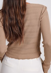 Top a maniche lunghe a costine, marrone, caratterizzato da un motivo a strisce testurizzato, orlo scallop e design aderente. Adatto per essere indossato a strati.