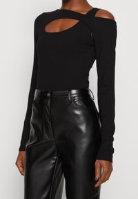Top nero a maniche lunghe a costine con dettaglio a taglio e spalle scoperte, abbinato a pantaloni in pelle nera a vita alta con cintura.