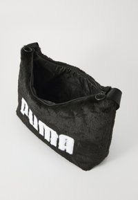 Svart faux fur håndveske med glidelås, har en innvendig fôr og en fremtredende hvit "PUMA"-logo på forsiden.