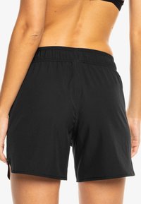 Sorte treningsshorts med elastisk midje, glatt tekstur og skreddersydd passform. Har sidesplitt for økt bevegelighet.