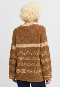 Maglione marrone a maglia caratterizzato da un materiale testurizzato e peloso con motivi geometrici color crema e una vestibilità rilassata. Maniche lunghe e scollatura arrotondata.