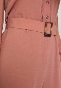 Vestido de tela texturizada color óxido con hebilla rectangular de carey y cinturón de tela a juego en la cintura, detalle de frontal abotonado.