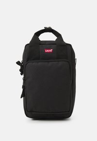 Crni ruksak napravljen od izdržljive tkanine s prednjim džepom na patentni zatvarač, gornjom drškom za nošenje i malim crvenim Levi's logotipom sprijeda.