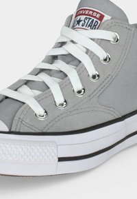 Κοντινό πλάνο ενός γκρι sneaker Converse All Star ψηλού τύπου με λευκά κορδόνια και λαστιχένια σόλα με λεπτομέρειες μαύρης ρίγας.