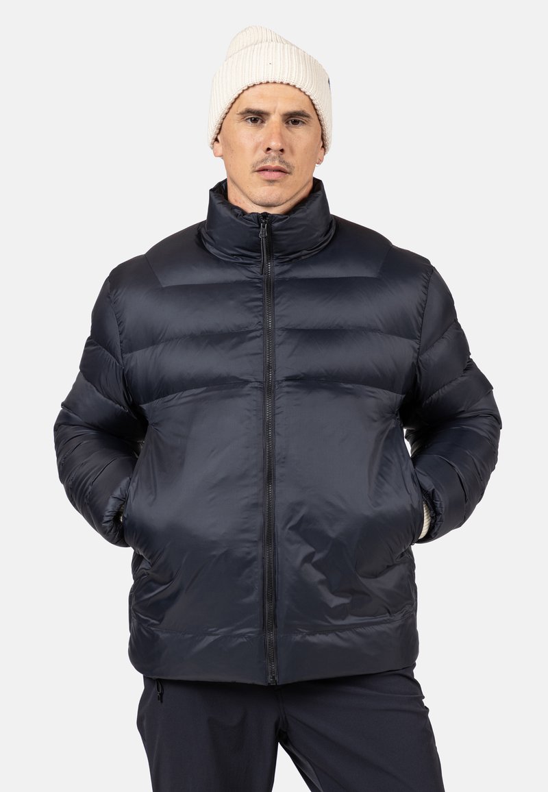 Giacca invernale blu navy con colletto alto, chiusura frontale con zip e design trapuntato con una texture liscia e lucida. Decorata con tasche laterali.