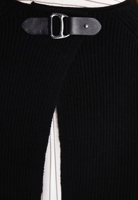 Schwarzes gestricktes Kleidungsstück mit vertikaler Rippstruktur, das an der Halslinie mit einem Lederriemen und einer metallischen Schnalle versehen ist.