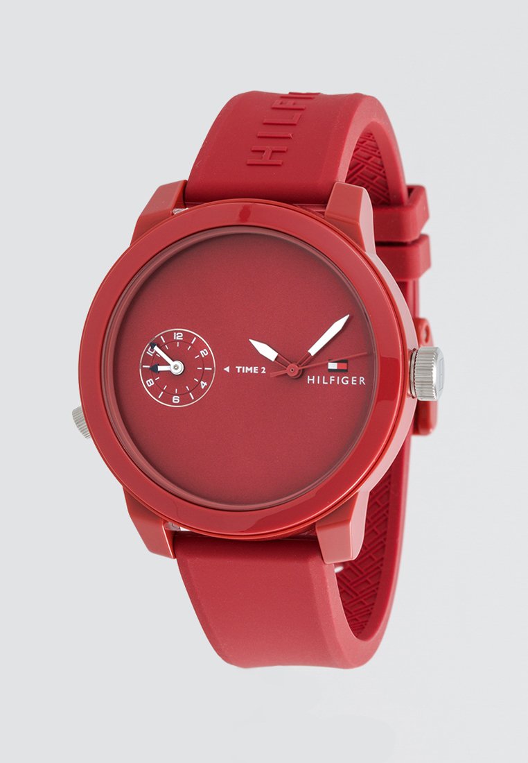 Reloj de silicona rojo con una esfera redonda, diseño minimalista y dos subesferas. Cuenta con una corona plateada y el logotipo de la marca en relieve en la correa.