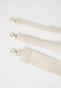 Three beige straps with gold metal clips; materials include textured leather and soft fabric, one strap features a logo and varied widths.