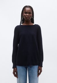 Laivastonsininen neulepaita veneaukkokauluksella ja pitkillä hihoilla, jossa on rento leikkaus. Yhdistetty vaaleansinisien farkkujen kanssa. Sileä pinta.