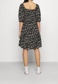 Schwarzes Blumenkleid mit quadratischem Ausschnitt, Puffärmeln und geraffter Taille, mit einem ausgestellten Rock, der von rosa und grünen Blumen akzentuiert wird.
