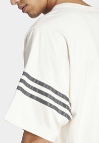 Cream-colored t-shirt with a crew neck, featuring a textured gray stripe design on the sleeve and a relaxed fit.