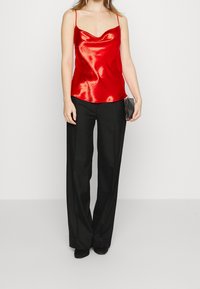 Camiseta de satén rojo con tirantes finos, escote drapeado; combinada con pantalones negros de cintura alta y un clutch negro. Textura suave, acabado brillante.