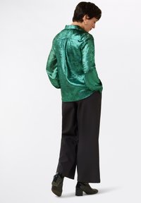 Smaragdgroene, shirt met metallic textuur, met een kraag, lange mouwen en een losse pasvorm, gecombineerd met zwarte wijde broek en hoge laarzen.
