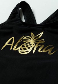 Svart tyg med en slät textur som har "Aloha" i guldmetallisk skrivstil och en ananasgrafik. Tunn remmar upptill.