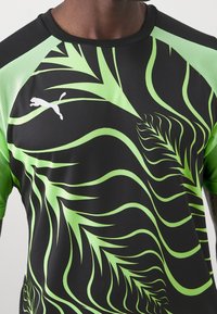 Svart atletisk kortärmad tröja med grön bladmönstrad design. Har en rund halsringning och texturerade gröna accenter på axlarna.