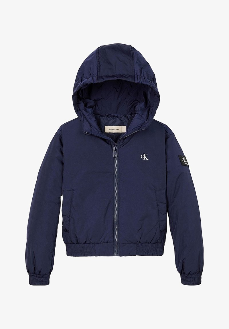 Giubbotto imbottito blu navy con cappuccio, zip frontale, polsini e vita elasticizzati. Presenta un piccolo logo bianco sulla spalla sinistra. Tessuto liscio.