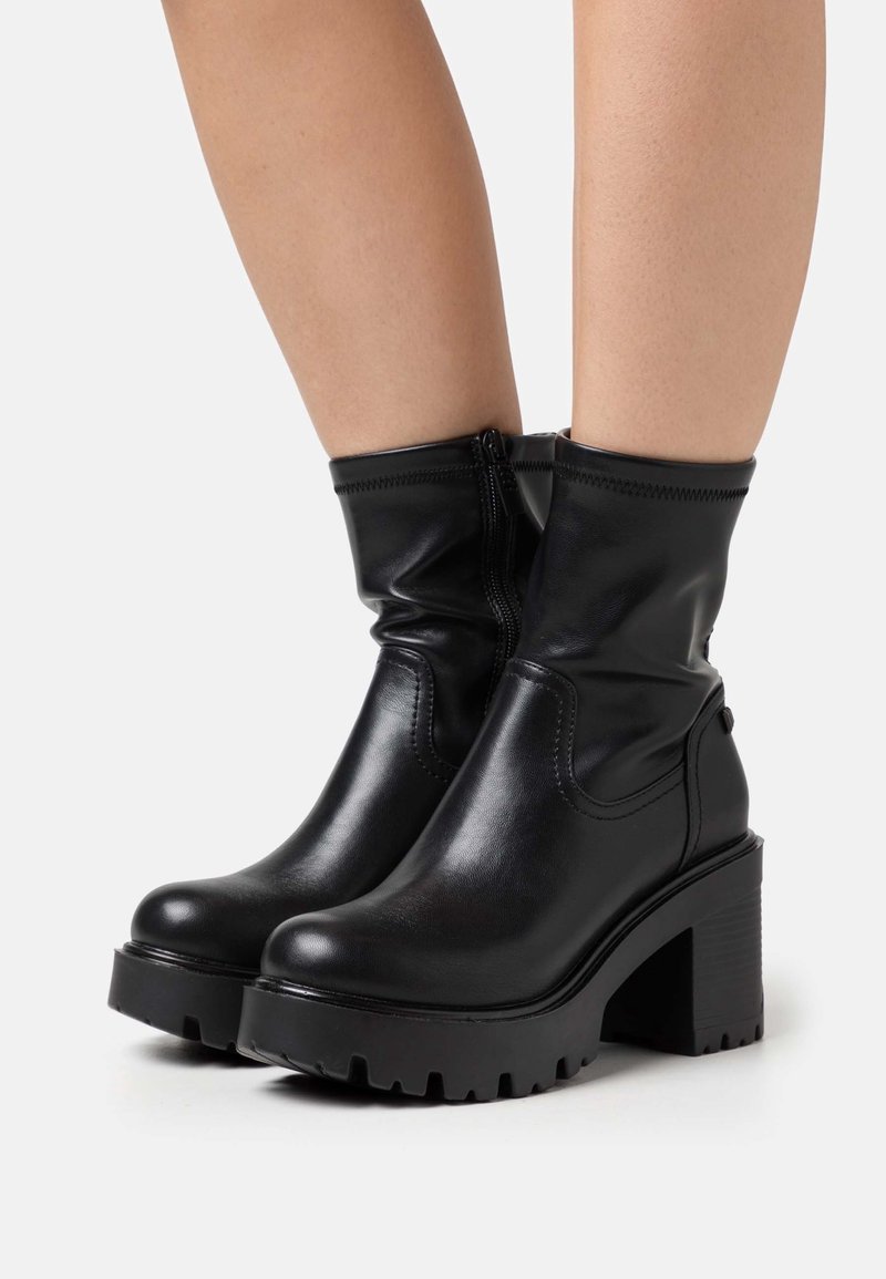Bottes noires à cheville avec un design élégant en cuir synthétique, semelle plateforme épaisse et fermeture éclair latérale. Tige texturée et rembourrée pour un confort optimal.
