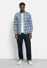 Blau-weißes kariertes Hemd mit langen Ärmeln und Knopfverschluss. Getragen über einem weißen T-Shirt mit dunklen Jeans und weißen Sneakern.