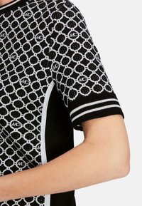 Das gestrickte schwarz-weiße Kurzarmshirt weist ein kreisförmiges Muster mit Logodetails auf und hat ein kontrastierendes weißes Seitenpaneel sowie einen gestreiften Saum.