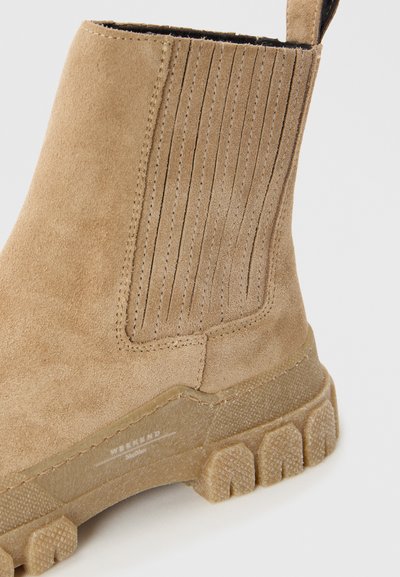 Stivale alla caviglia in suede beige con pannelli laterali a coste e una suola in gomma spessa e testurizzata. Presenta una linguetta per un facile indossamento.