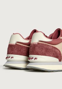 Ett par röda och gräddfärgade mockaskor med vita sulor, visade bakifrån mot en enkel ljus bakgrund.