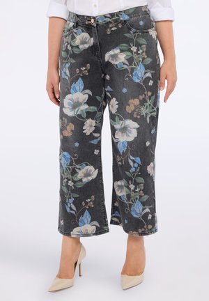 Czarne dżinsy o szerokich nogawach z dużym niebiesko-białym floralnym nadrukiem, noszone z beżowymi szpilkami i białą koszulą z podwiniętymi rękawami.