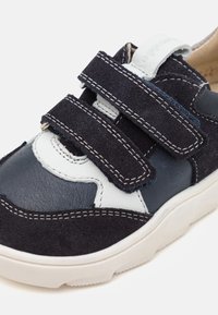 Blå og marineblå lær- og semsket skinn-sneakers med tre borrelåser, beige detaljer, hvit søm og en teksturert hvit såle.