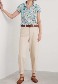 Chemise à manches courtes avec col, motif coloré, pantalon beige taille haute, et chaussures marron à brides avec une surface texturée.