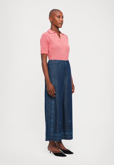 Polo shirt a righe rosse e bianche, abbinato a culottes di jeans con motivi decorativi blu. Indossato con scarpe slip-on nere a punta.