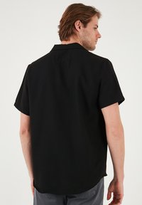 Camisa negra de manga corta con un corte relajado, que presenta un cuello y una tela suave. La parte posterior es lisa con detalles de dobladillo curvado.