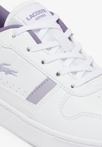 Baskets blanches avec des accents violets, design à lacets, matériau en cuir texturé, détails perforés sur les côtés et logo sur le côté.