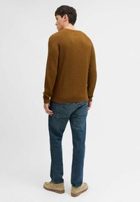 Braun gerippter Strickpullover, lockere Passform, Rundhalsausschnitt. Kombiniert mit blauen Jeans und beigen Schuhen. Minimalistisches und texturiertes Aussehen.