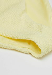 Maillot de bain jaune avec un tissu texturé, doté d'une doublure intérieure lisse et d'un bord tressé. Le design est cohérent et doux au toucher.