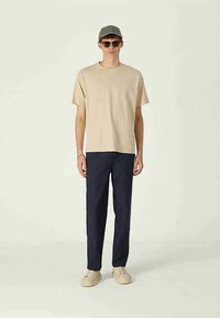 Beige cotton t-shirt, navy trousers, mesh cap, and shades, with beige sneakers. Simple design, relaxed fit, and minimal details.