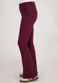 Slim-fit donker bordeauxrode broek met voor- en achterzakken, gedragen met beige en maroon casual schoenen, zijaanzicht.
