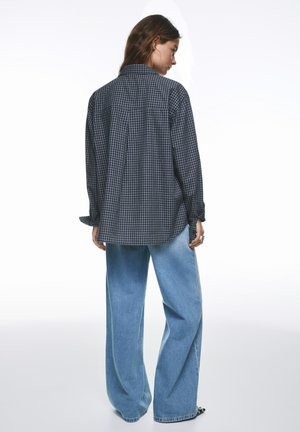 Čierno-biela károvaná košeľa na gombíky s dlhými rukávmi, štýlovo skombinovaná so svetlomodrými širokými džínsami. Má voľný strih a zaoblený okraj.