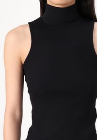Svart ribbet ermeløs turtleneck-topp med høy krage og tettsittende design, laget av et mykt, stretchy stoff.