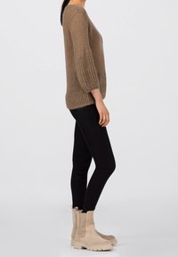 Brązowy dziergany sweter o pudełkowym kroju z prążkowanymi rękawami, zestawiony z czarnymi spodniami o wąskim kroju i beżowymi botkami za kostkę.