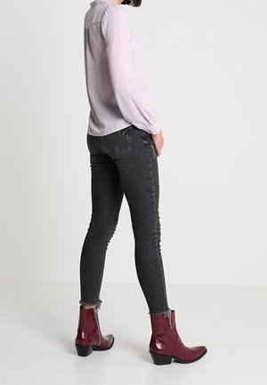 Blouse violet clair à manches longues, associée à un jean skinny gris foncé avec des ourlets effilochés et des bottines bordeaux brillantes à enfiler.