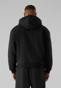 Haut à capuche noir avec cordon de serrage, ourlet et poignets côtelés. Fabriqué en tissu doux et texturé. Le design présente une coupe décontractée.
