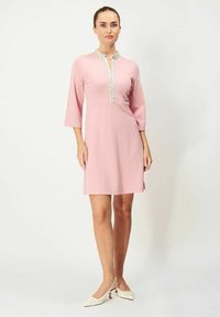 Kort rosa klänning med mandarinkrage, trekvartslånga ärmar och dekorativa silverdetaljer längs fram. Slät tygtextur.