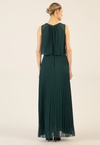 Langes, plissiertes Abendkleid in Dunkelgrün, mit einer transparenten Überlage am Oberteil, ärmellosem Design und einem fließenden Rock.