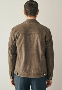 Bruine suède jas met een soepele textuur, voorzien van een klassieke kraag en knoopsluiting bij de mouwen. Eenvoudig ontwerp met minimale details.