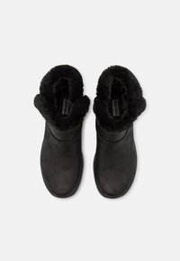 Botas negras hasta el tobillo hechas de cuero suave con forro de piel sintética en el cuello y suela de goma plana. Diseño minimalista sin herrajes visibles.